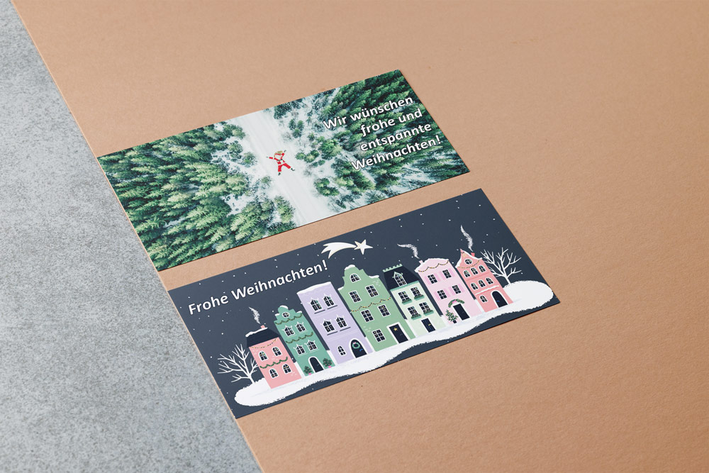Weihnachtskarten für das Architekturbüro Eisenbraun und Eisenbraun Immobilien mit dem Thema "Entspannung". Eine Karte zeigt einen entspann auf dem Rücken liegenden Weihnachstmann im verschneiten Wald, die andere Karte zeigt eine verschneite, friedvolle Häuserreihe in den Firmenfarben.